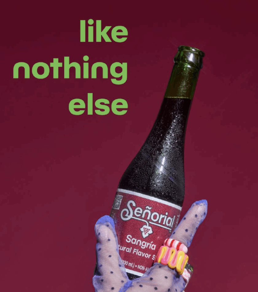 A hand wearing sheer polka-dot gloves holds a chilled Señorial Sangría soda bottle against a bold maroon background with the phrase ‘like nothing else.