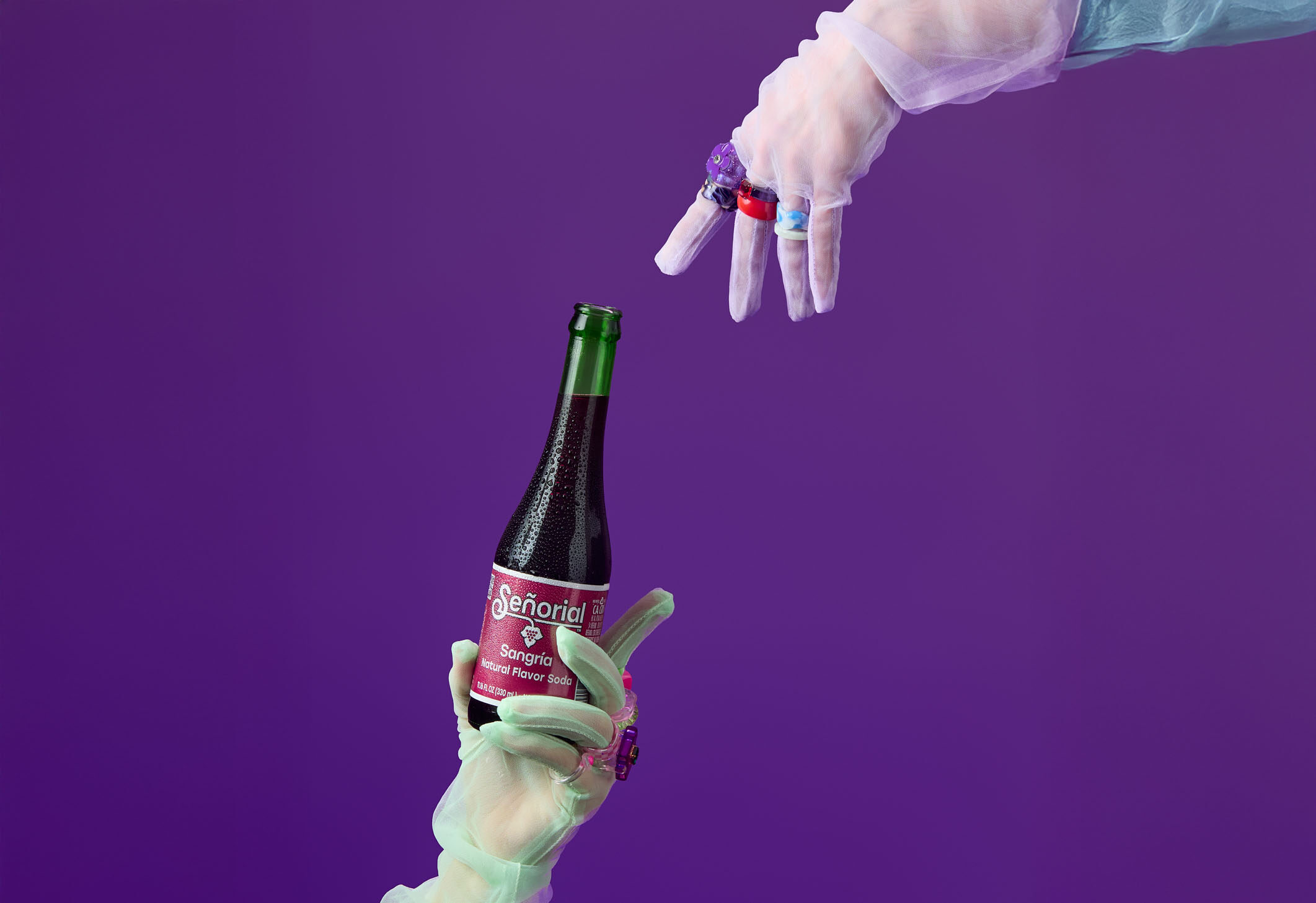 Gloved hands presenting a chilled Sangría Señorial bottle against a bold purple background.