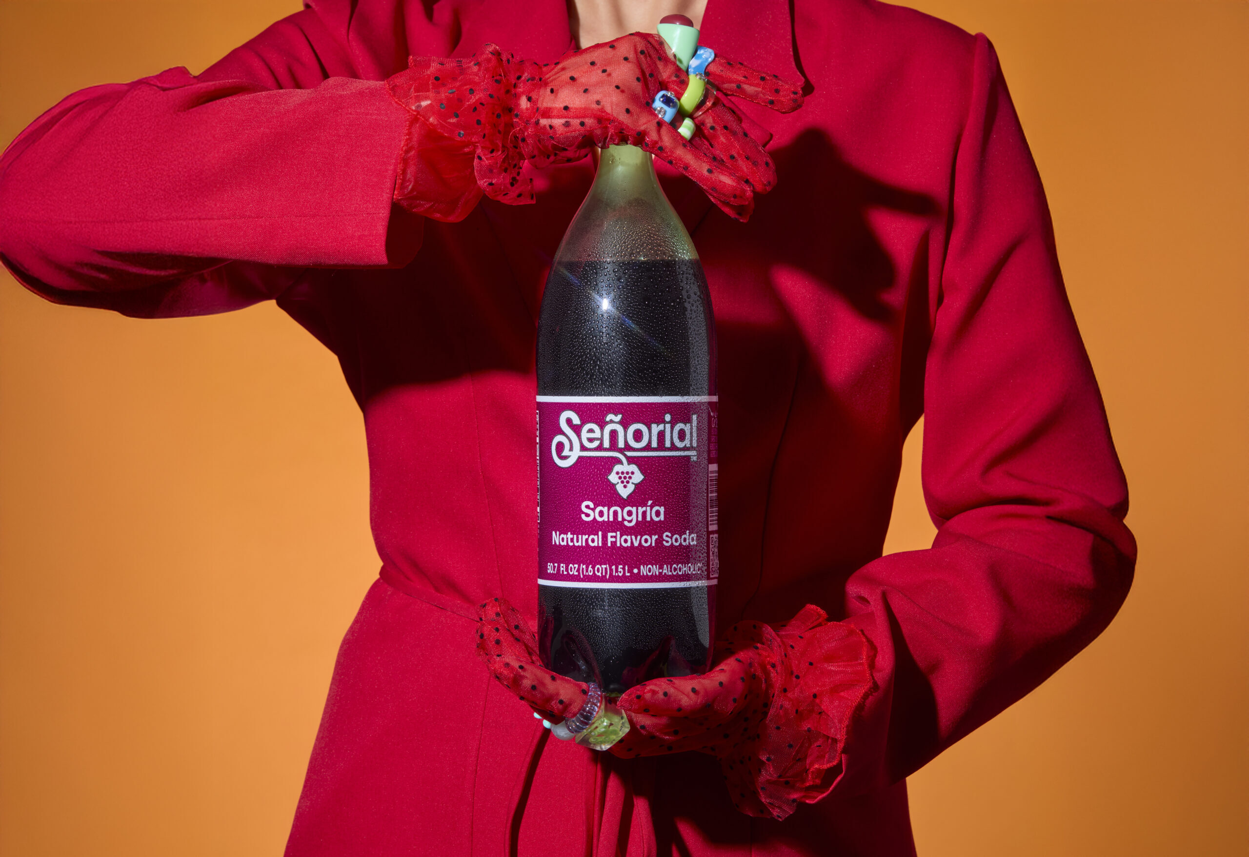 Person in vibrant red holding a large Sangría Señorial bottle against a warm orange backdrop, creating a bold and striking presentation.