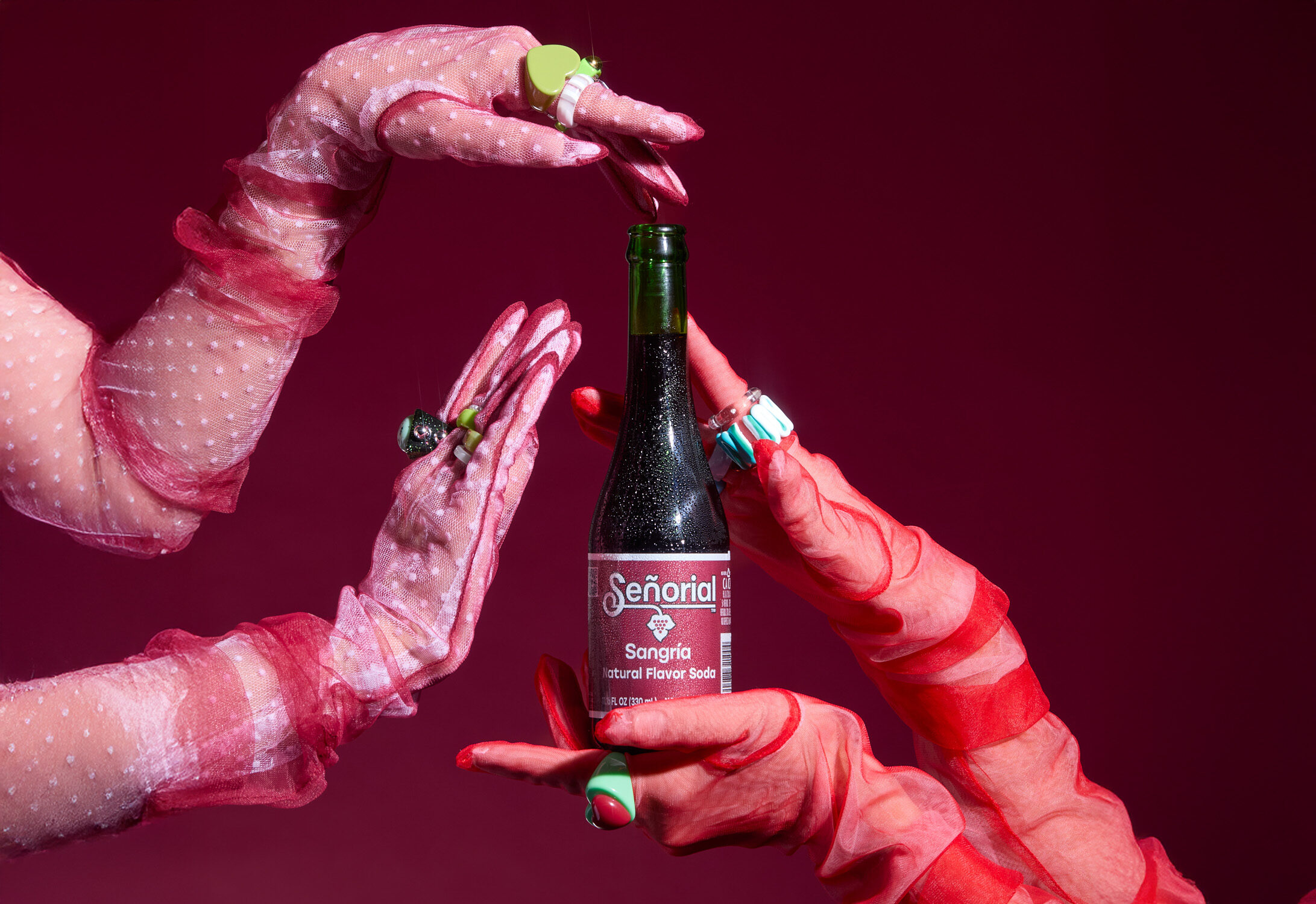 Gloved hands elegantly framing a Sangría Señorial bottle against a rich red background, highlighting the drink with a bold, artistic touch.