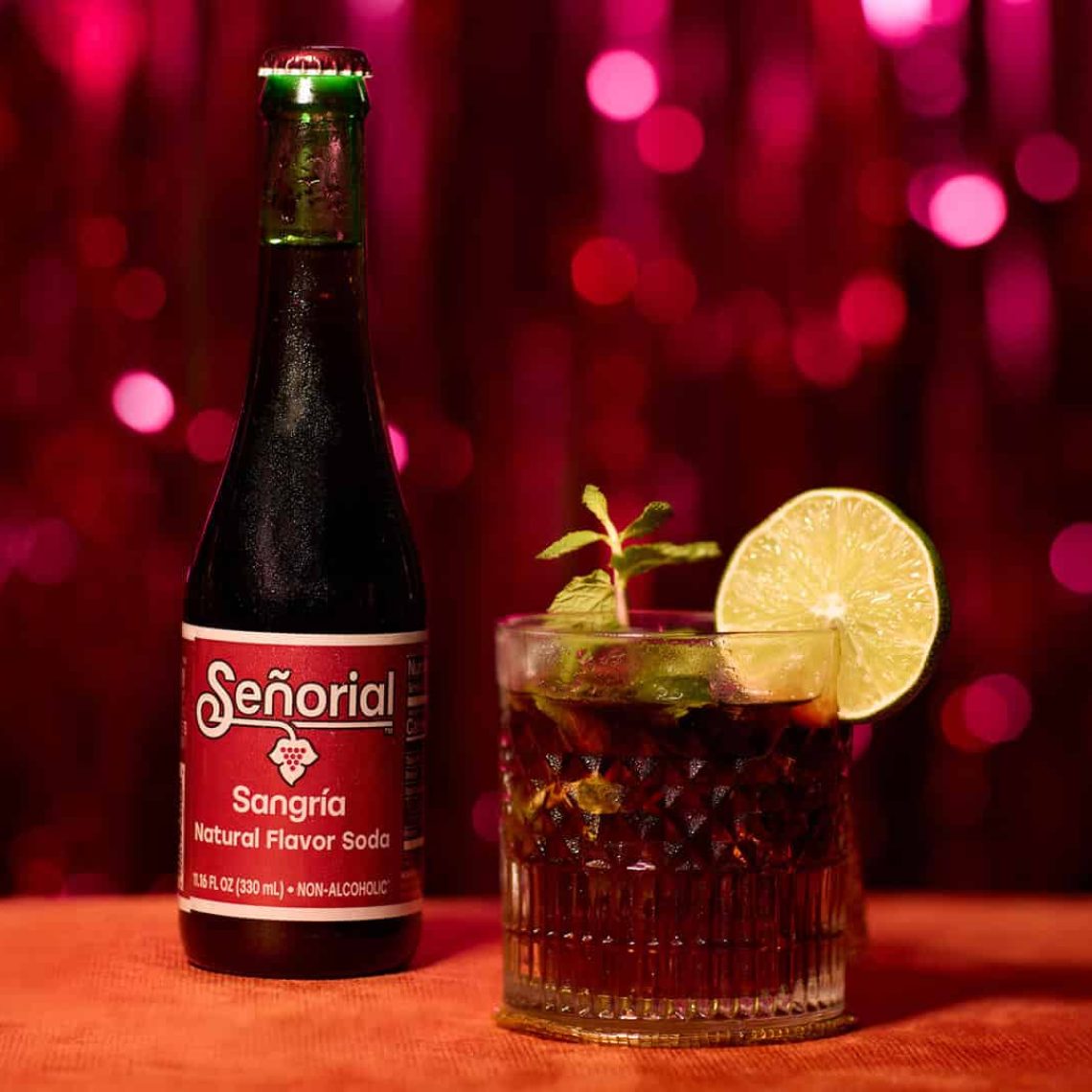 Sangria Senorial bottle paired with an iced mocktail garnished with lime and mint, styled as a bold, premium non-alcoholic drink moment.
