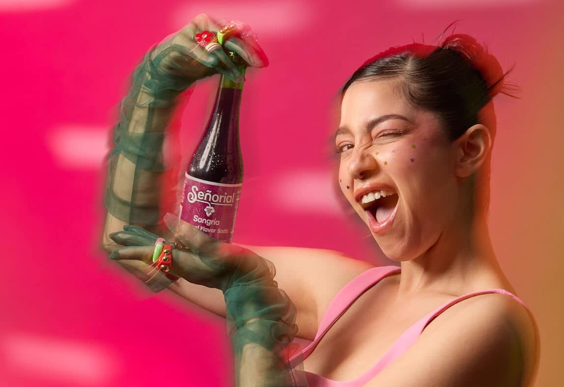 Playful lifestyle shot featuring Sangria Senorial soda bottle held with bold expression, vibrant colors, and energetic styling for a modern, refreshing brand moment.