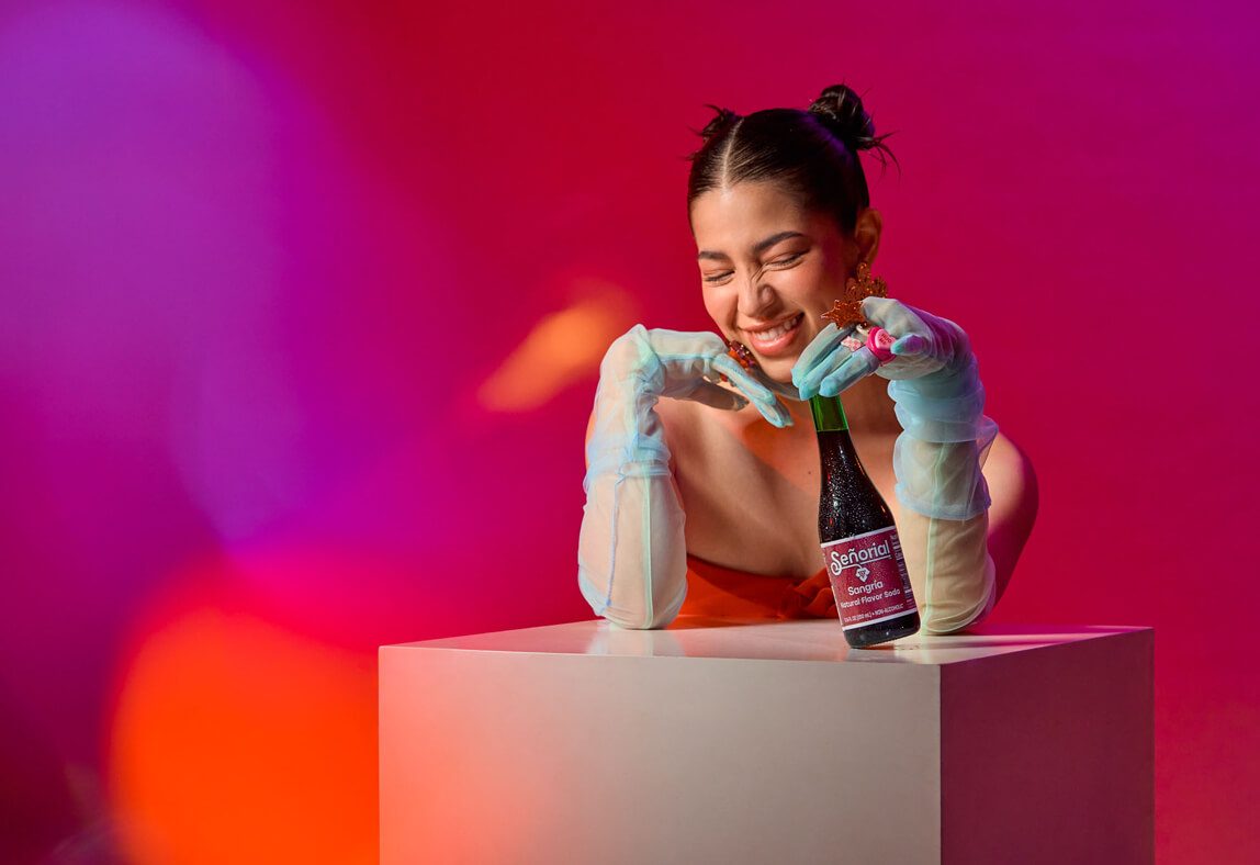 Playful lifestyle portrait with a Sangria Senorial bottle, showcasing vibrant color, joyful expression, and a modern premium non-alcoholic vibe.