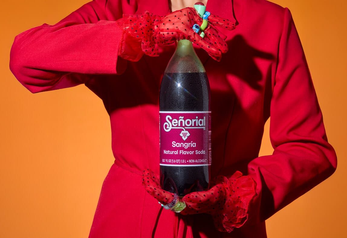 Stylish hands presenting a Sangria Senorial bottle against a warm background, highlighting bold design and a premium non-alcoholic soda.