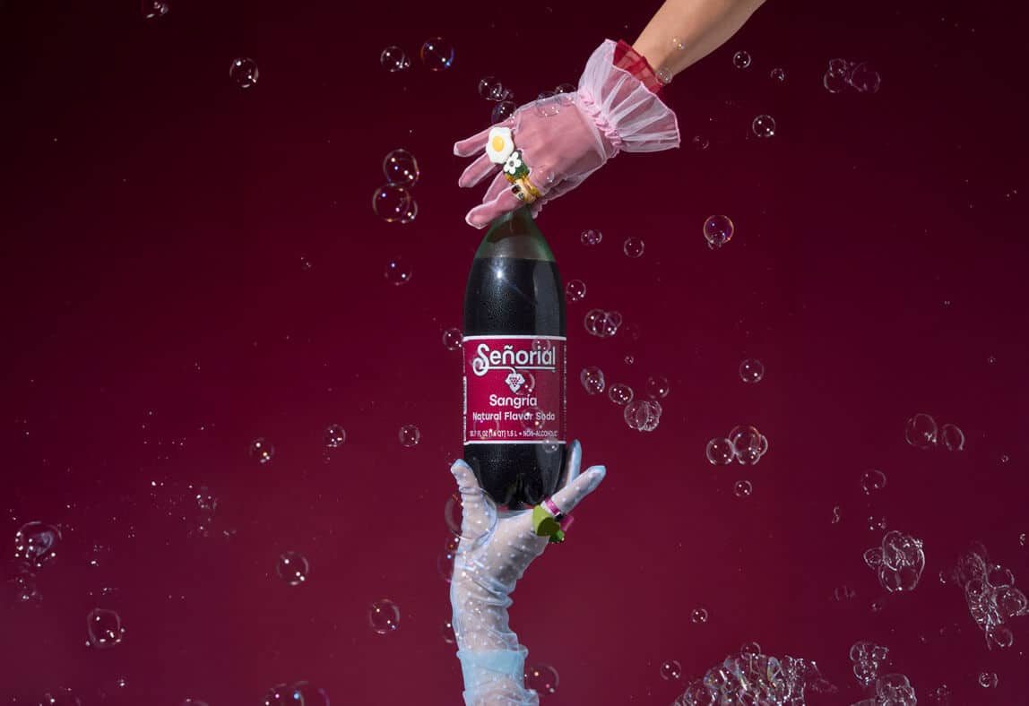 Hands presenting a Sangria Senorial bottle surrounded by bubbles, highlighting a playful, refreshing, and premium non-alcoholic brand moment.