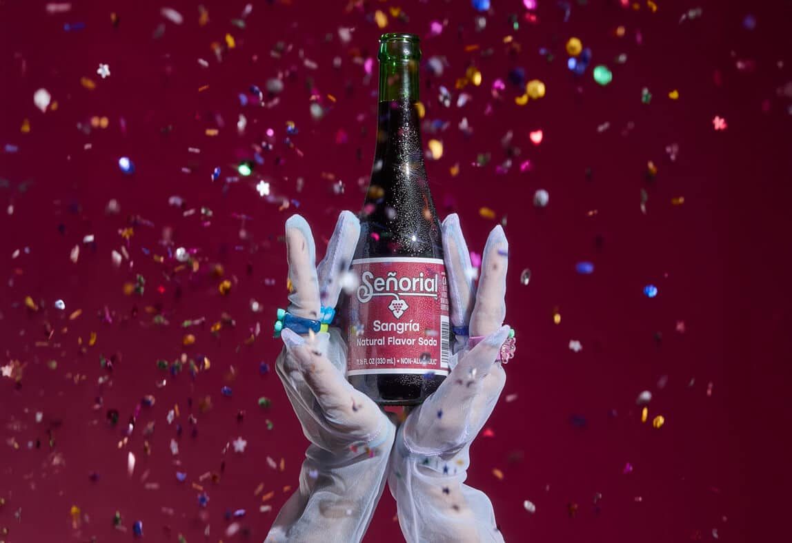 Sangria Senorial bottle held by gloved hands amid falling confetti, capturing a festive, bold, and premium non-alcoholic celebration.
