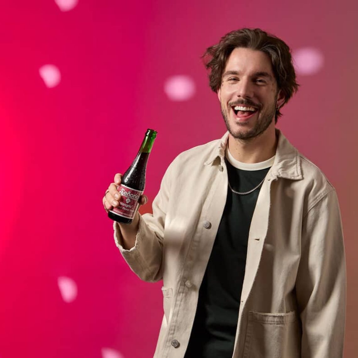 Smiling person holding a Sangria Senorial bottle, showcasing a relaxed, vibrant, and premium non-alcoholic brand moment.