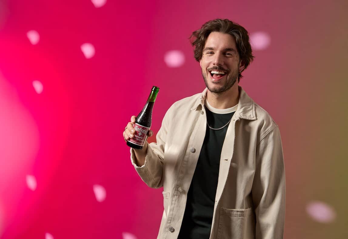 Smiling person holding a Sangria Senorial bottle, showcasing a relaxed, vibrant, and premium non-alcoholic brand moment.