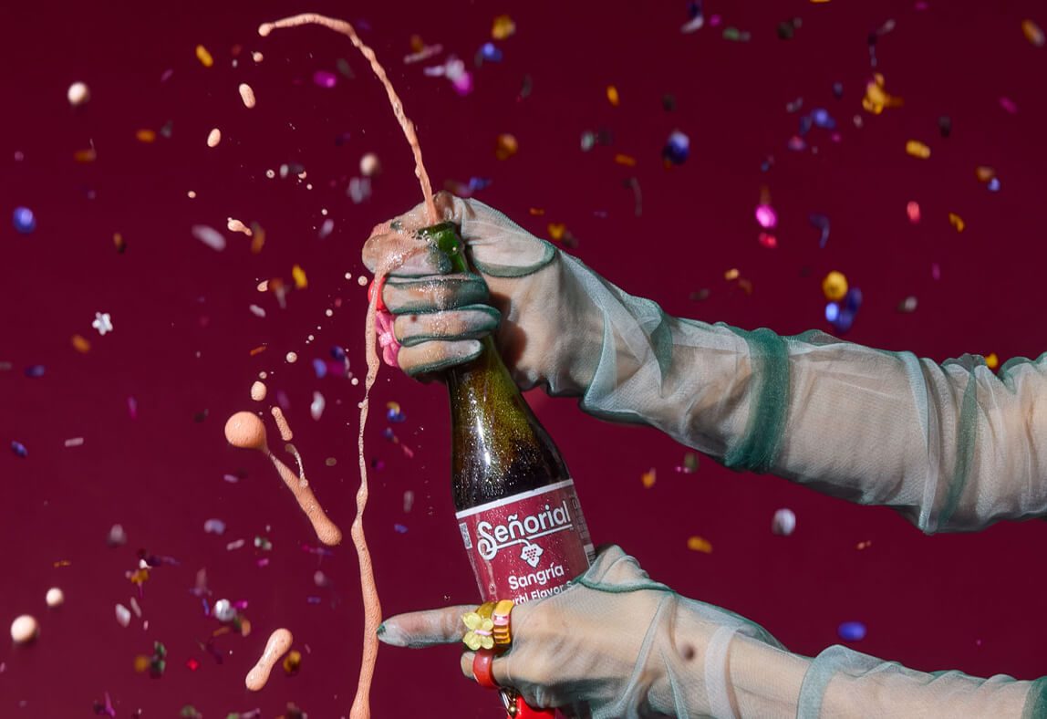 Sangria Senorial bottle opening with a dynamic splash, surrounded by confetti, capturing an energetic and celebratory non-alcoholic moment.